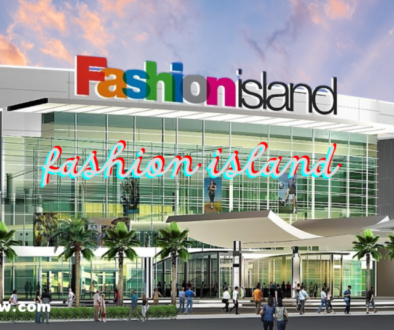 An exterior view of a shopping center named "Fashion Island," with a colorful logo at the top of the building. Below, there are glass windows, palm trees, and people walking around the entrance.